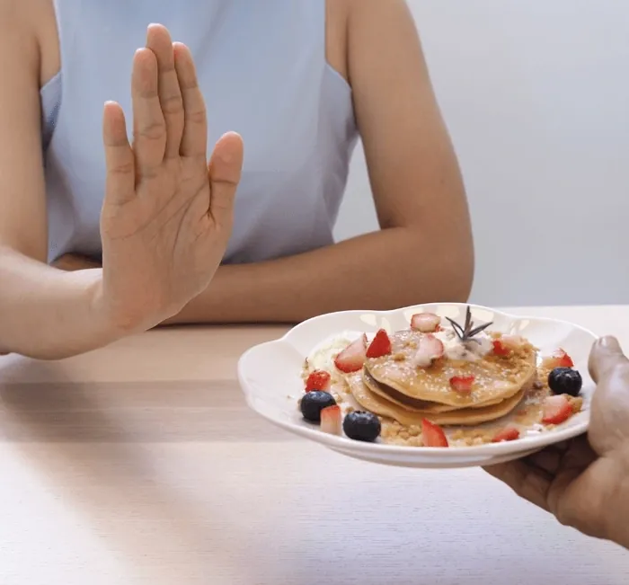 A woman pushing away a plate of pancakes (brand artwork)
