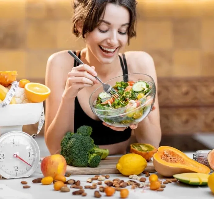 A woman eating a salad with fruit and vegetables (brand artwork)